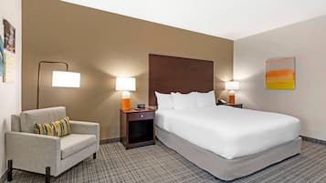 A hotel room with a bed, a chair, two bedside tables with lamps, a wall with a painting, and a patterned carpet.