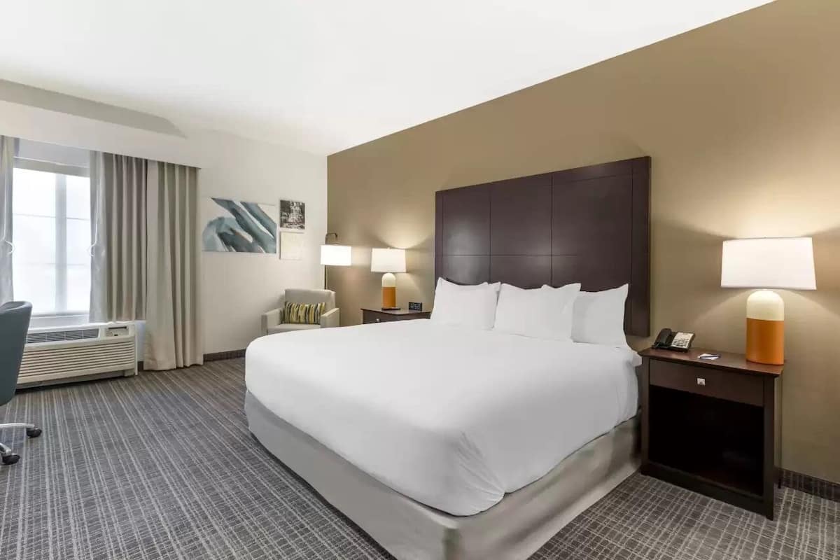 Una habitación de hotel con una cama grande, dos mesitas de noche con lámparas, una silla, un escritorio y una ventana con cortinas.