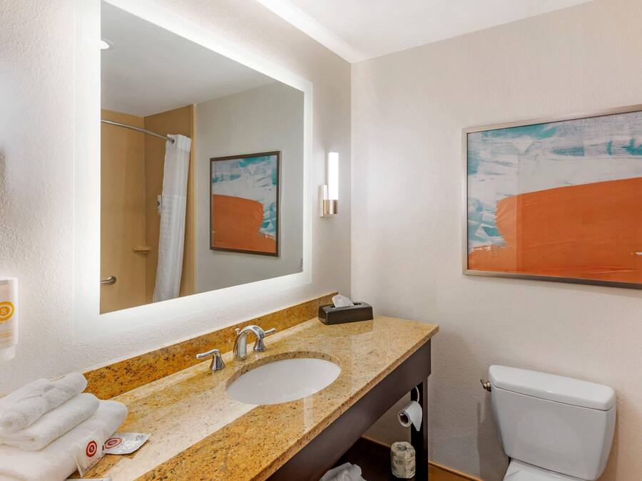 A bathroom with a sink, mirror, towel rack, toilet, and a framed abstract painting on the wall.