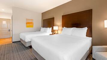 A hotel room with two beds, a nightstand with a lamp, a painting on the wall, and a door.