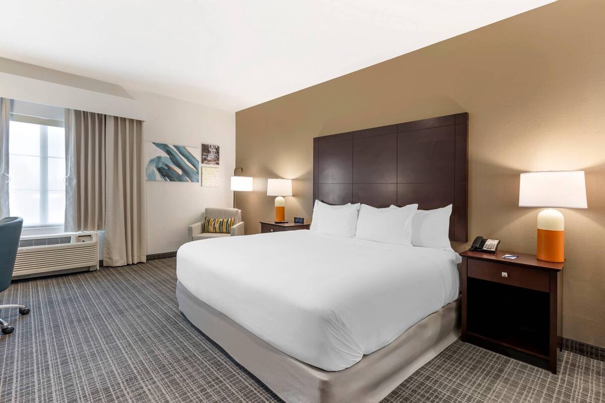 Una habitación de hotel con una cama grande, dos mesitas de noche con lámparas, una silla, un escritorio y una ventana con cortinas.