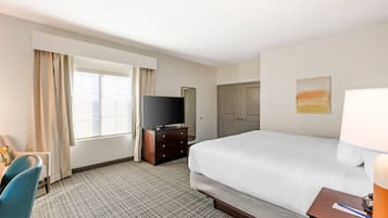 Quarto de hotel com uma cama, uma televisão em uma cômoda, uma escrivaninha com cadeira e uma janela com cortinas.