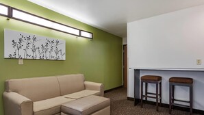 A room with a beige sectional sofa, a wall-mounted artwork, two barstools, and a white counter.