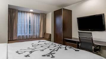 Quarto de hotel com cama, televisão fixada na parede, janela com cortinas e guarda-roupa.