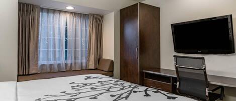 Une chambre d’hôtel avec un lit, un téléviseur fixé au mur, une fenêtre avec des rideaux et une armoire.