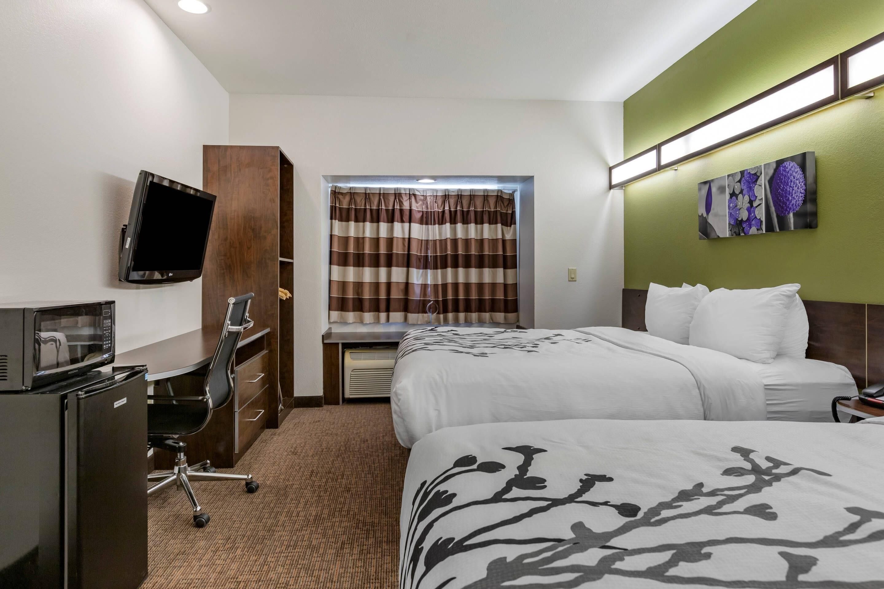 Hotelkamer met een bed, een bureau met een computer, een televisie, een magnetron, een stoel en een raam met gordijnen.