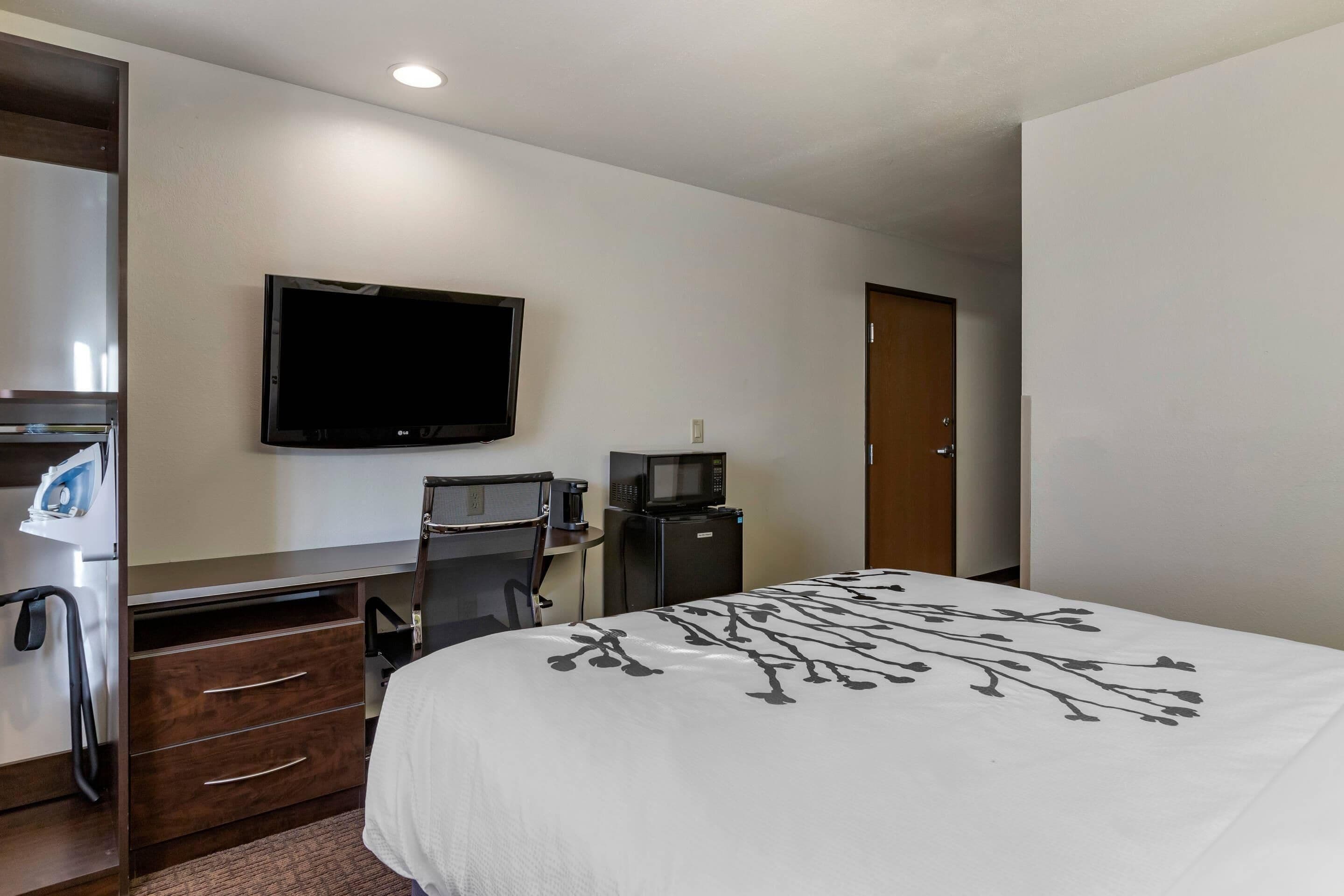 Habitación de hotel con cama, escritorio con computadora, televisor, microondas y cafetera.