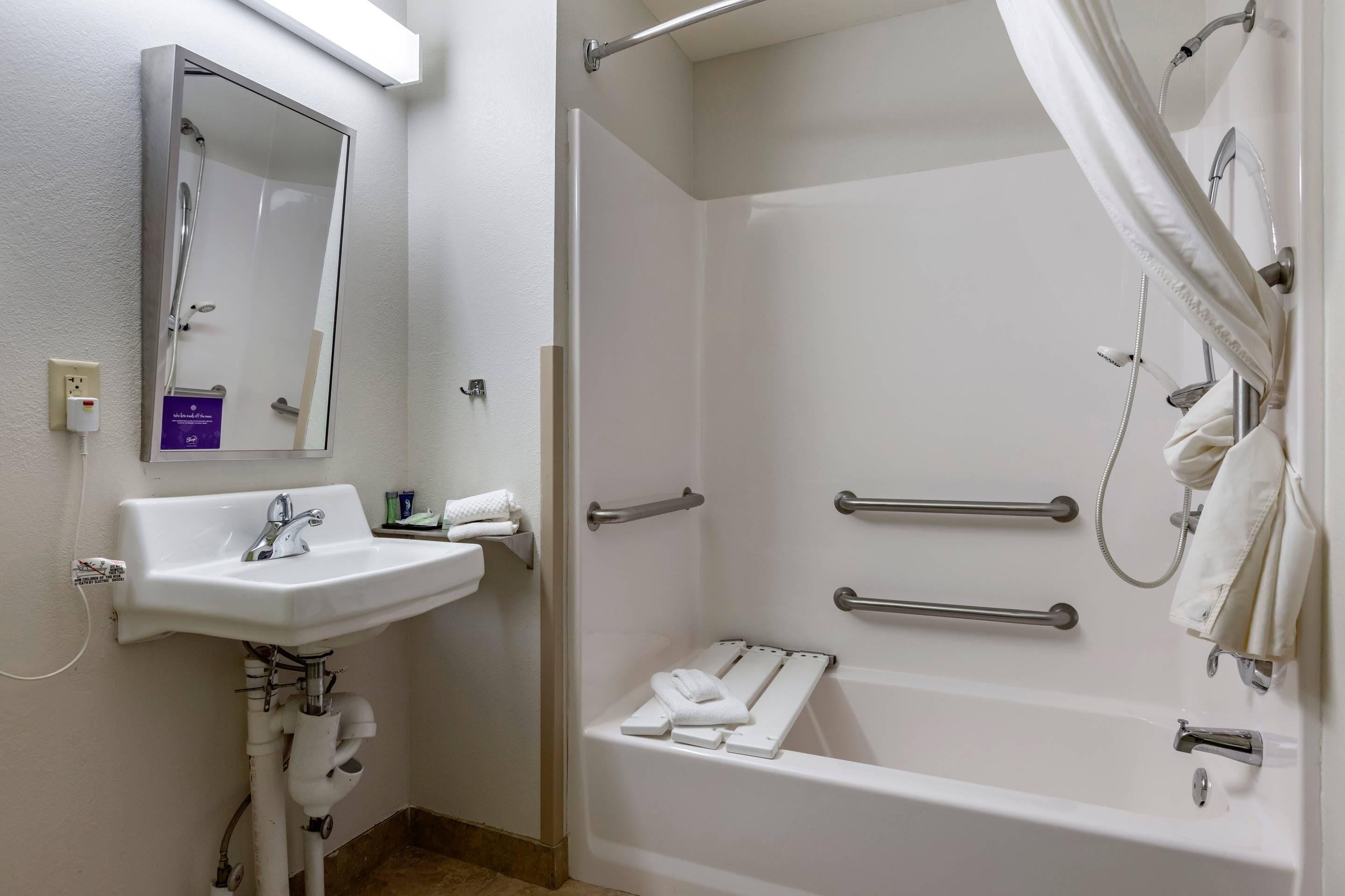 A bathroom with a sink, mirror, shower, and grab bars.