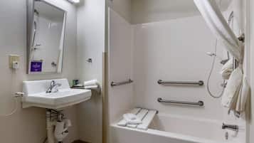 Un baño con lavamanos, espejo, ducha y barras de apoyo.