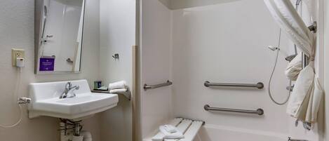 A bathroom with a sink, mirror, shower, and grab bars.