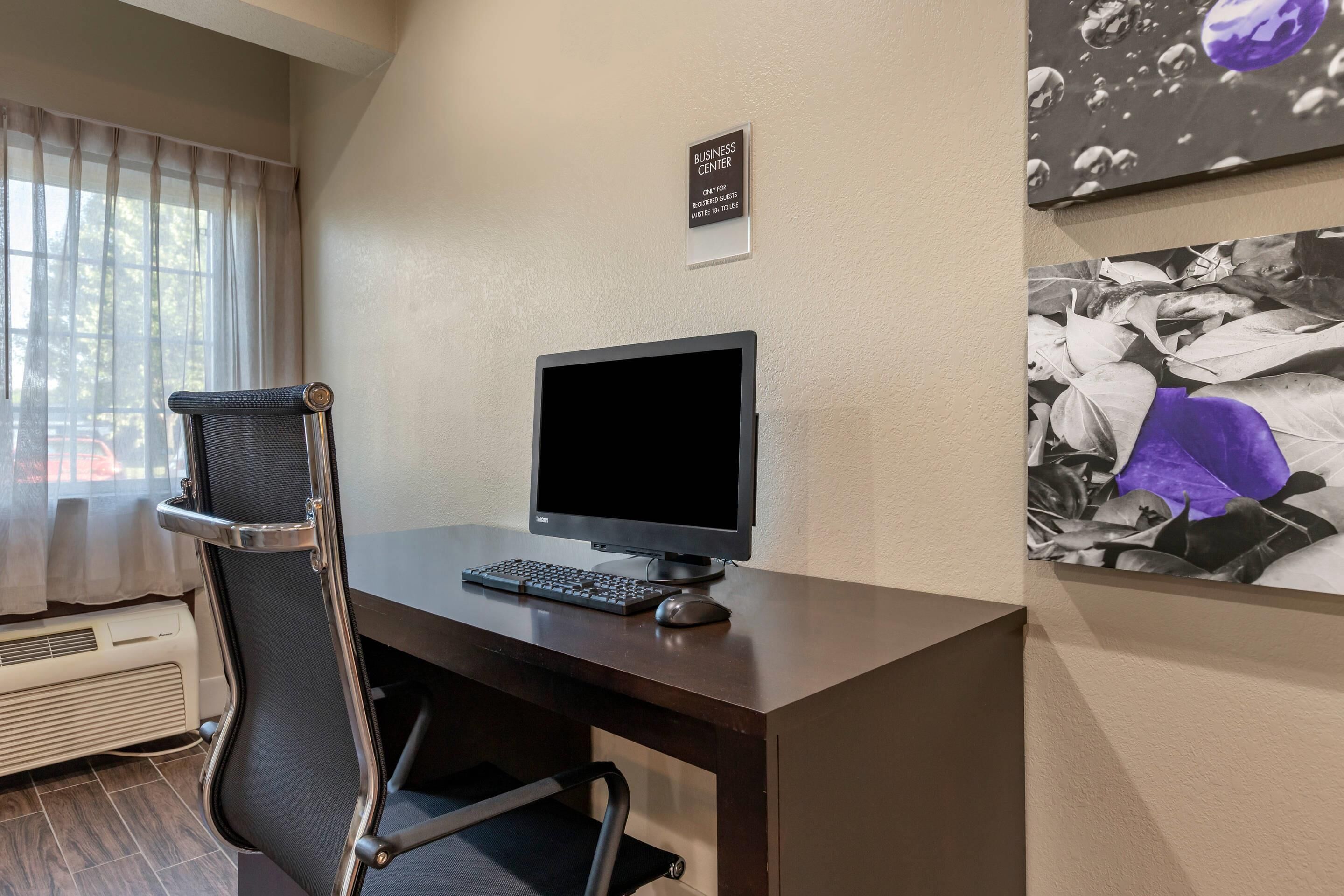 A hotel room with a desk, computer, chair, air conditioning unit, and a sign indicating the business center.