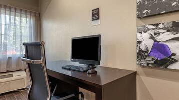A hotel room with a desk, computer, chair, air conditioning unit, and a sign indicating the business center.