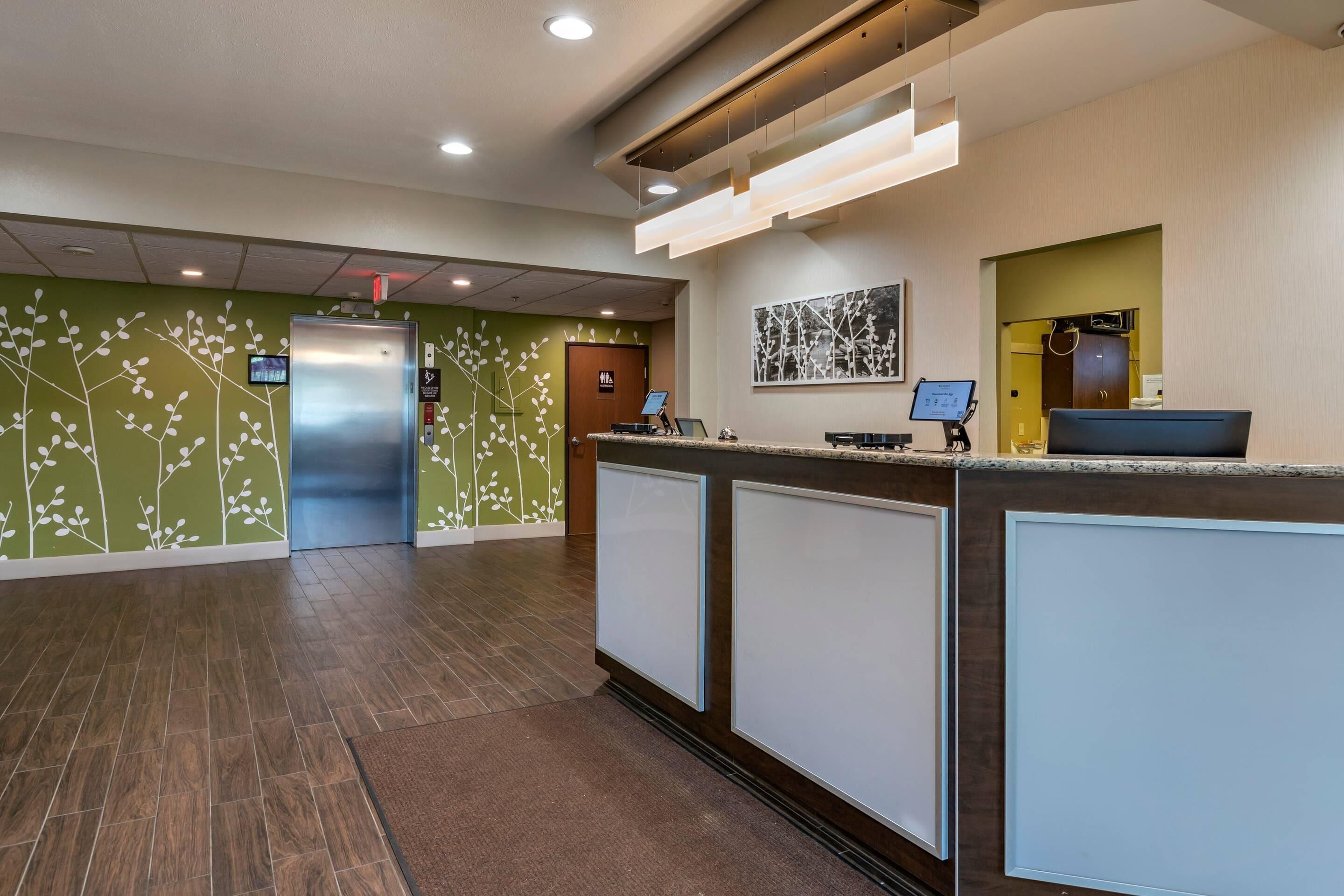 A reception area with a counter, a digital screen, a wall-mounted artwork, and a door leading to another room.