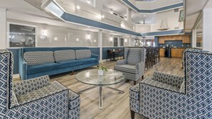 Un salón amplio con un sofá azul, sillones estampados, una mesa de centro de vidrio y una cocina al fondo.