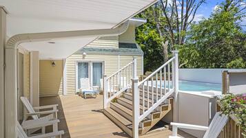 Um deck coberto com piso de madeira, corrimãos brancos e uma escadaria para uma área de piscina.