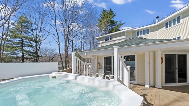 Una piscina con cubierta de madera, un patio techado y una casa de dos pisos con techo verde.