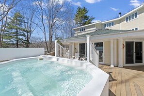 A swimming pool with a wooden deck, a covered patio area, and a two-story house with a green roof. - The Grand Hotel (Ogunquit)