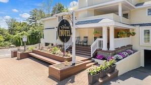 Un hotel con un letrero que dice "The Grand Hotel", que cuenta con un porche con escalones, asientos al aire libre y un jardín ajardinado.