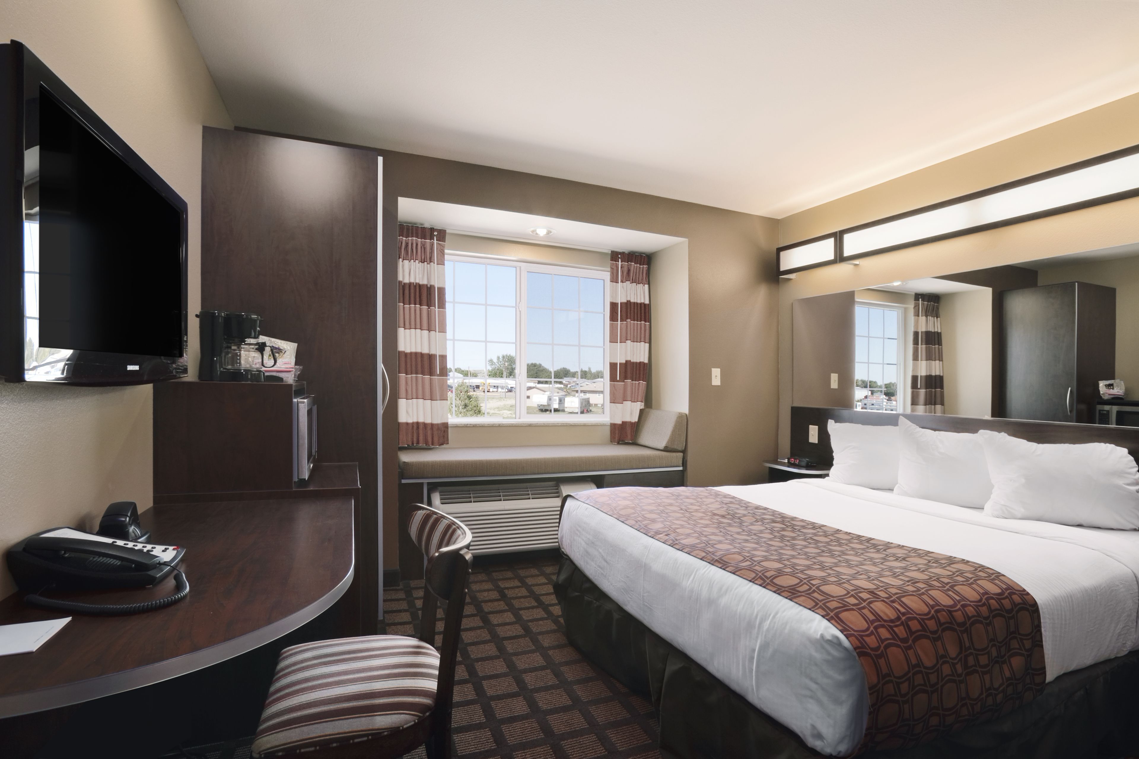 Une chambre d’hôtel comprenant un lit, un bureau avec un téléphone, une chaise, une fenêtre avec des rideaux et un téléviseur.