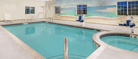 Une piscine intérieure ornée d’une fresque représentant une plage, avec un poste de surveillance pour les sauveteurs et un petit espace détente équipé de chaises.