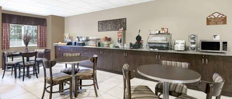 A hotel breakfast area with a counter, coffee machines, and seating.