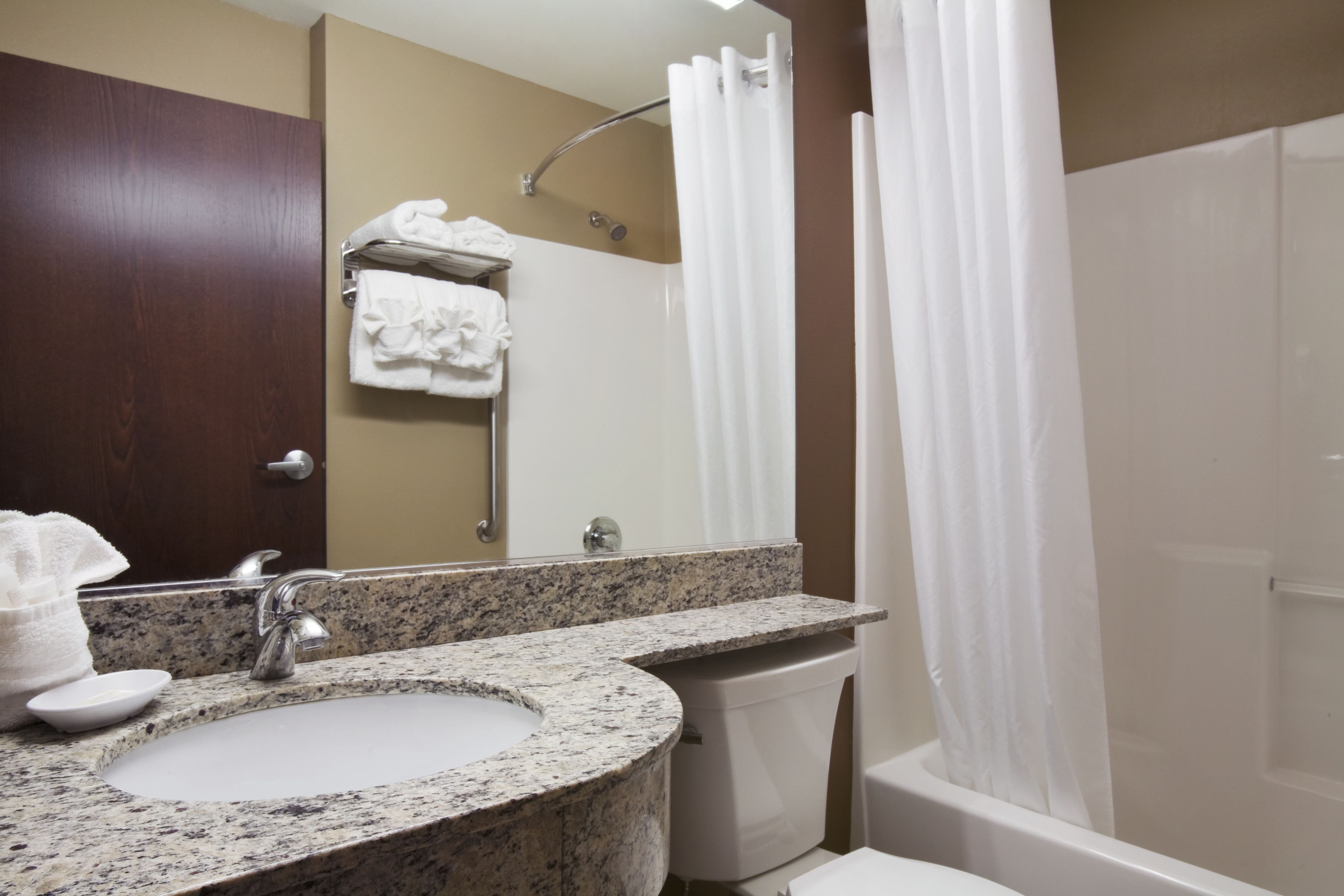 A bathroom with a granite sink, a mirror, a towel rack, a shower curtain, and a toilet.