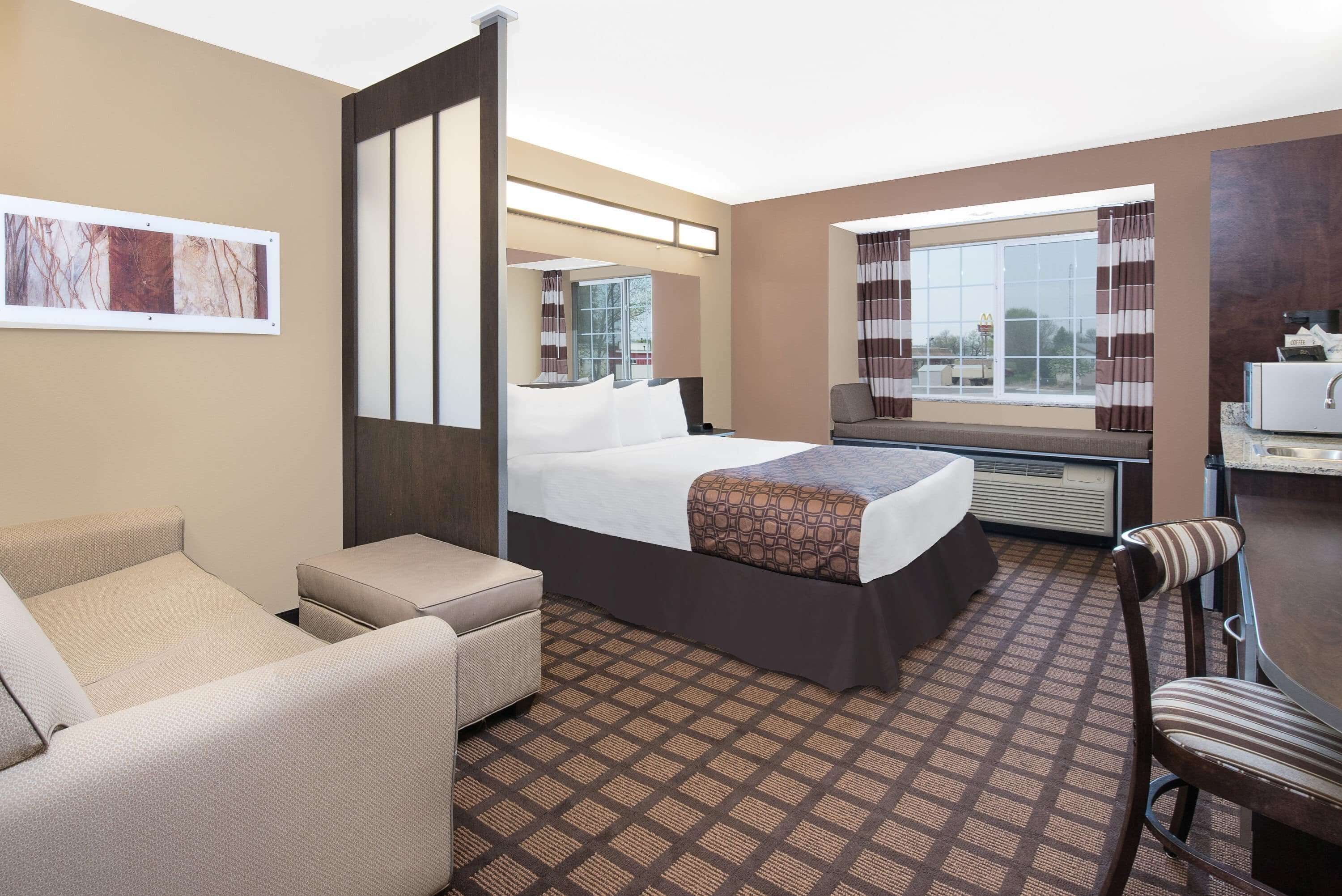 Une chambre d’hôtel comprenant un lit, un canapé, un bureau, une chaise, une fenêtre avec des rideaux et une œuvre d’art accrochée au mur.