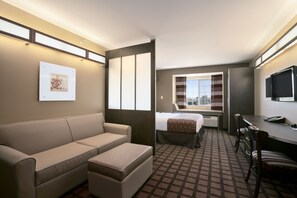 Een hotelkamer met een bank, een bed, een bureau met stoel, een televisie en een raam met gordijnen.
