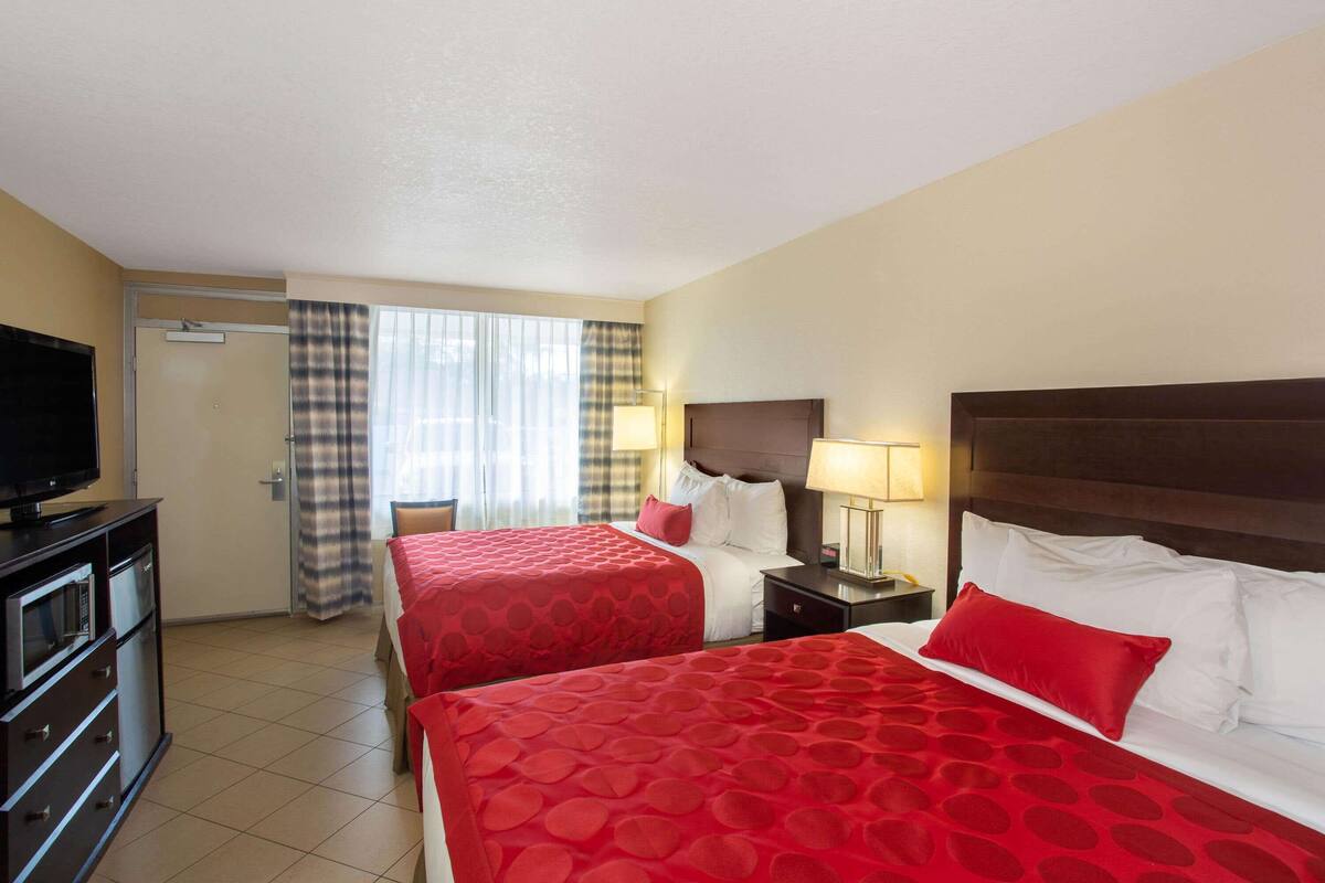Habitación de hotel con dos camas, un televisor, un escritorio y una ventana con cortinas.