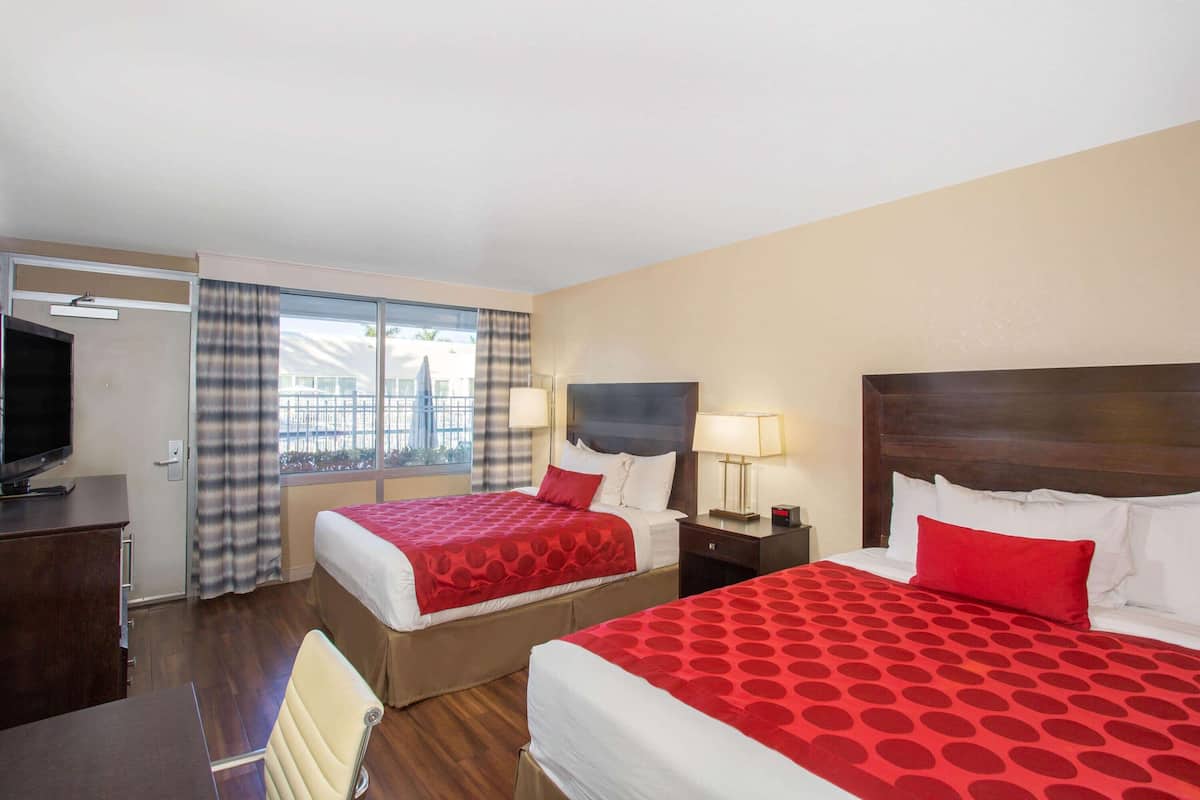 Habitación de hotel con dos camas, un escritorio, un televisor y una ventana con cortinas.
