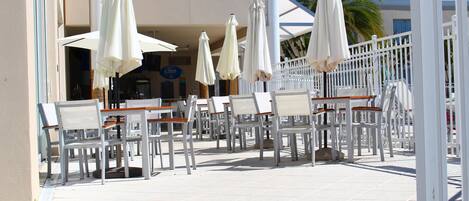 An outdoor seating area with white chairs and umbrellas, a white fence, and a building in the background.