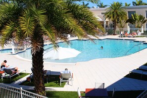 Área de piscina com espreguiçadeiras, uma palmeira e piscina azul cristalina.