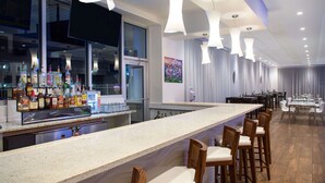 A bar area with a long counter, multiple stools, and a variety of liquor bottles. - Ramada by Wyndham Venice Hotel Venezia (Venice)