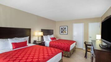 A hotel room with two beds, a desk, a chair, a TV, and a door.