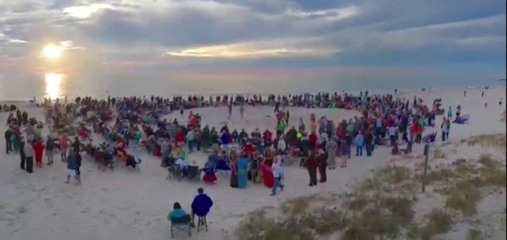 A beach with a large crowd gathered in the center, possibly for an event or gathering.