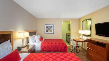 Habitación de hotel con dos camas, un escritorio, una silla, un televisor y un baño visible a través de una puerta abierta.