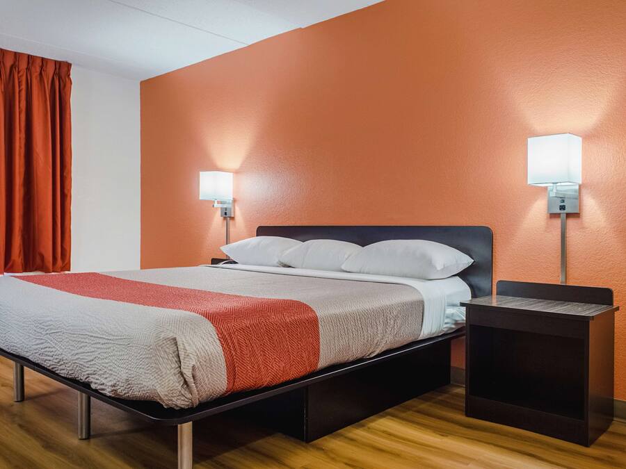 Une chambre d’hôtel avec un lit, deux tables de chevet et une lampe fixée au mur.