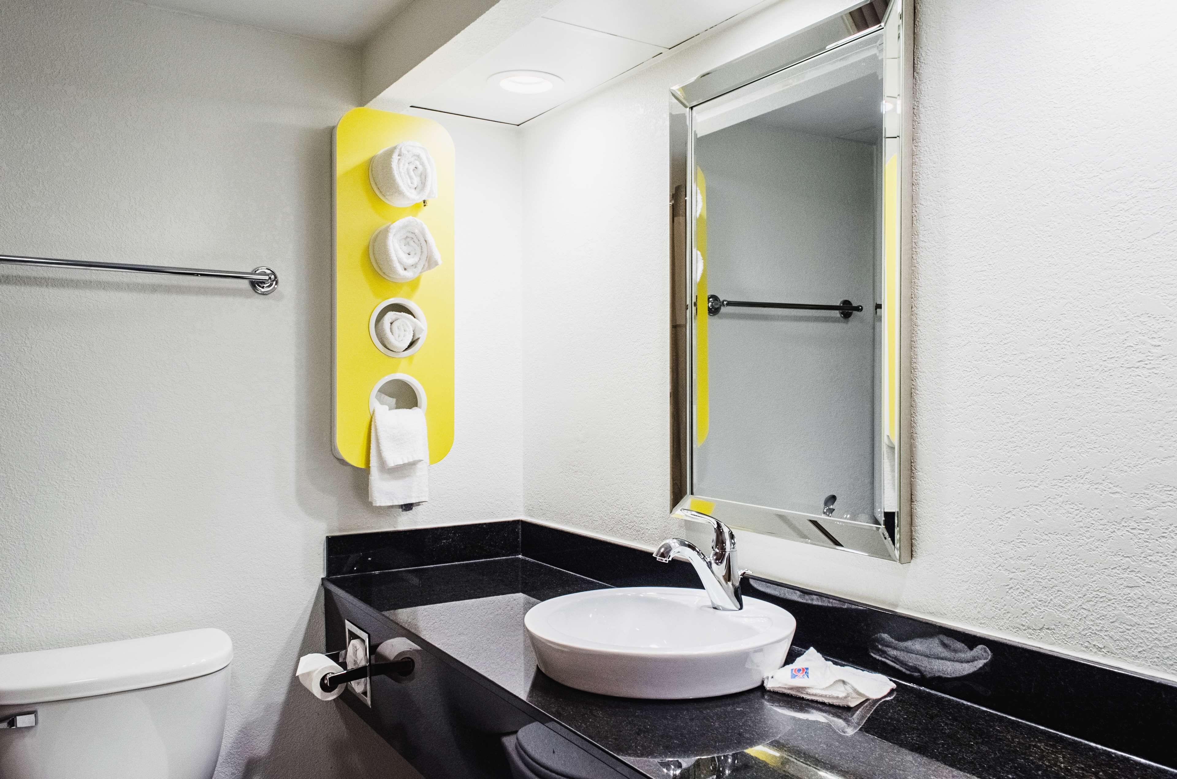 Un baño con inodoro blanco, lavabo negro, espejo y toallero amarillo.