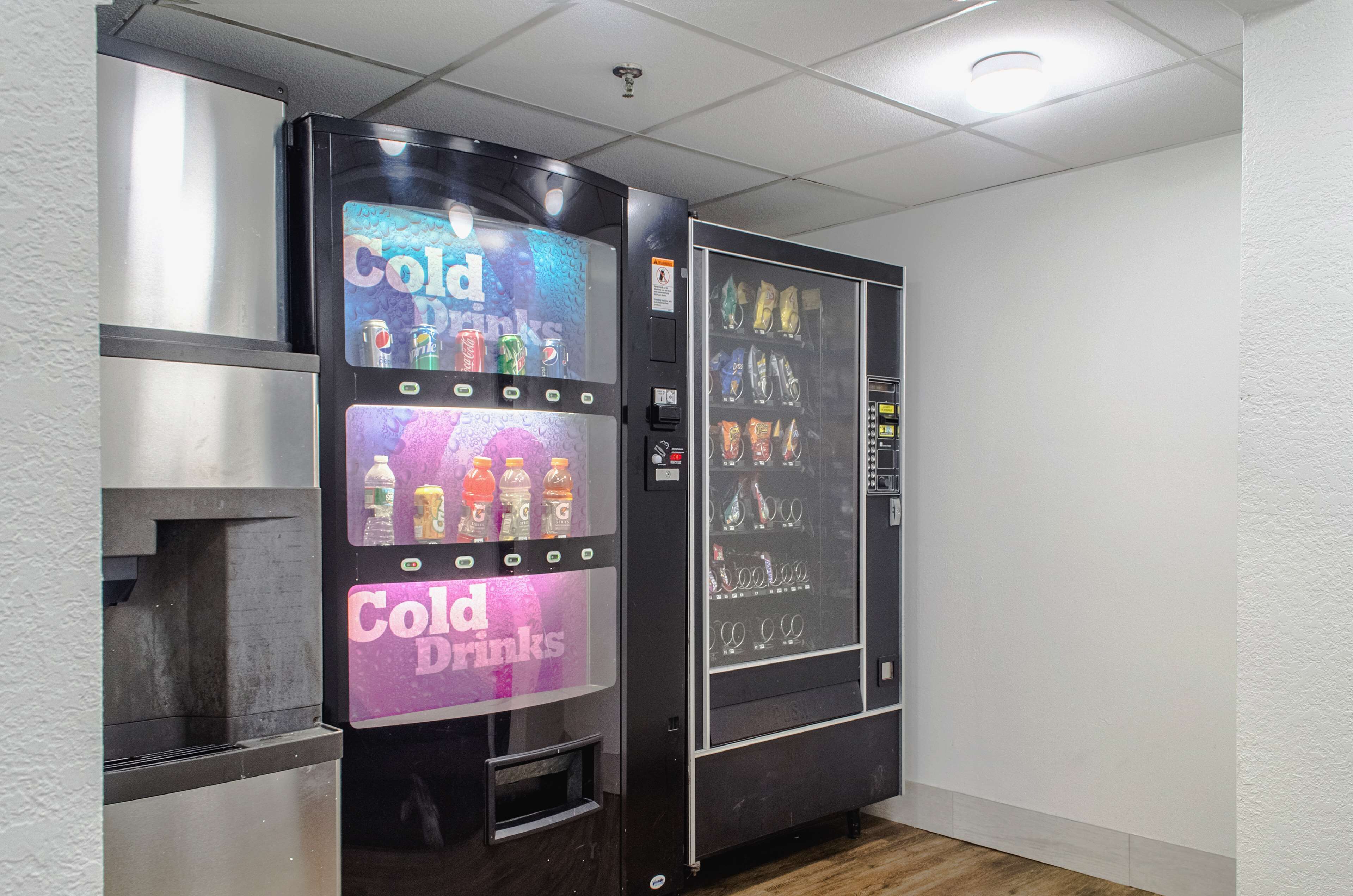Máquina expendedora con la etiqueta 'Cold Drinks' en una habitación con paredes blancas y suelo de madera.