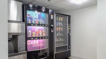 Máquina expendedora con la etiqueta 'Cold Drinks' en una habitación con paredes blancas y suelo de madera.