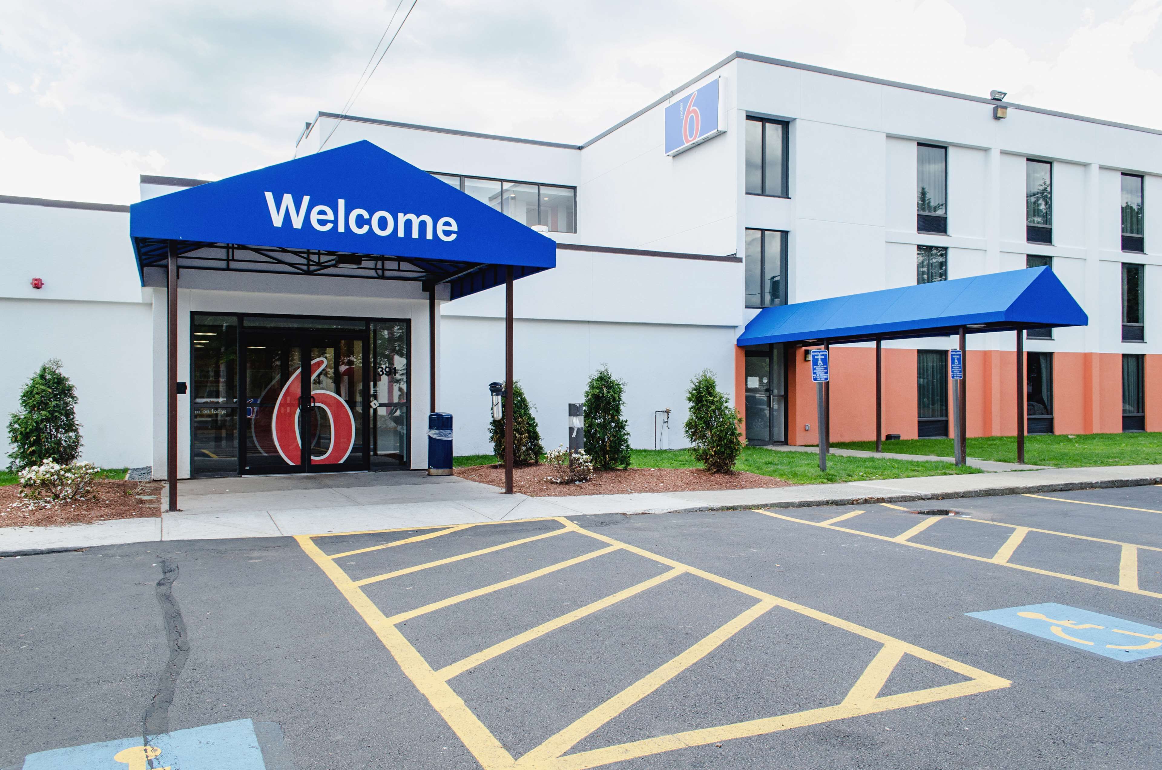 A modern building with a 'Welcome' sign, a parking lot with marked spaces, and a number '6' sign.