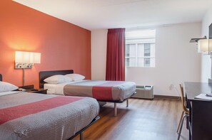 A hotel room with two beds, a desk, a chair, a window with curtains, an air conditioning unit, and a wall-mounted lamp. - Motel 6 Brockton, MA (Brockton)