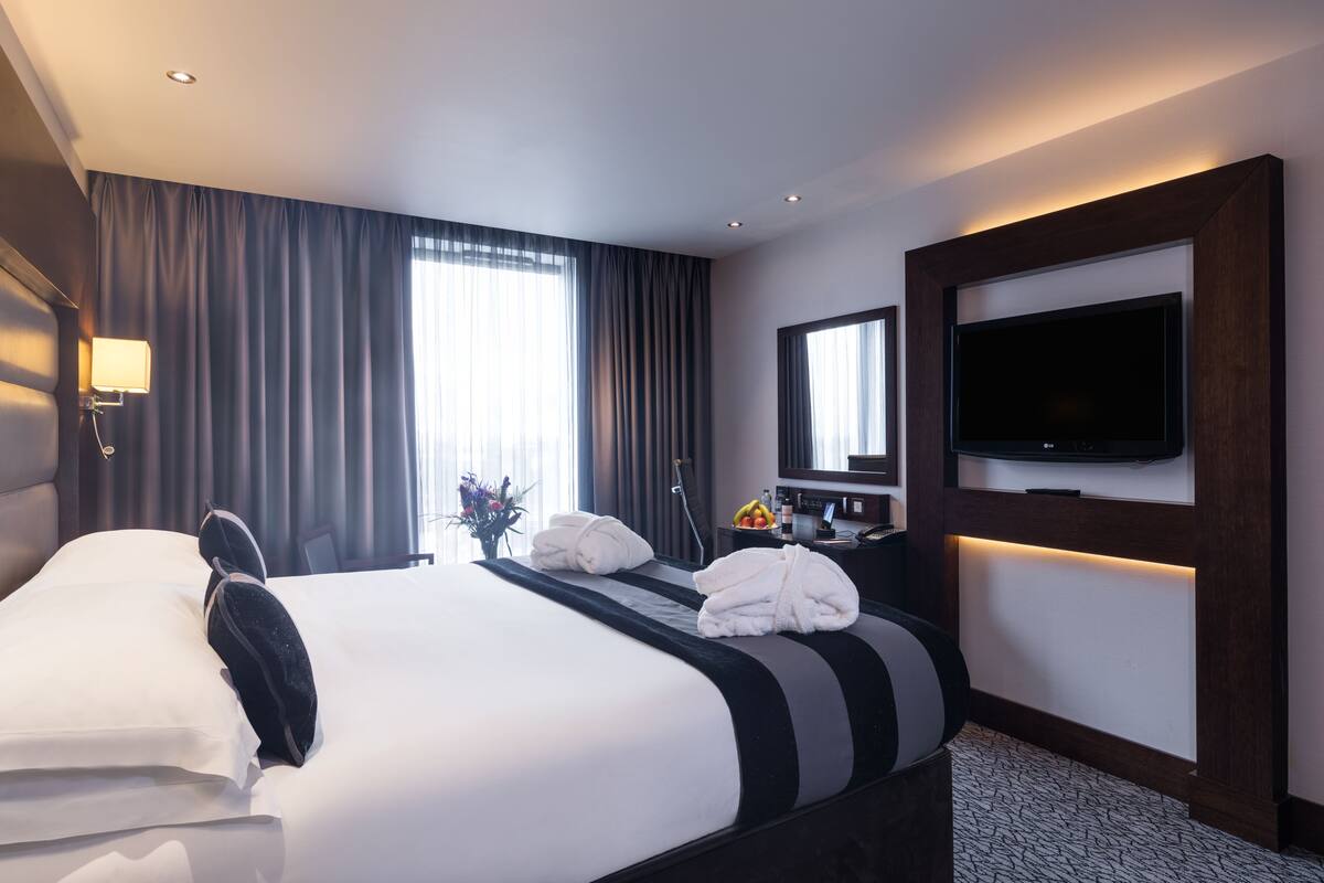 Een hotelkamer met een groot bed, een flatscreen televisie aan de muur, een bureau met een lamp en een raam met gordijnen.