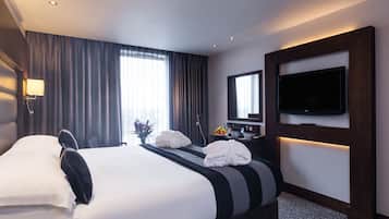 Een hotelkamer met een groot bed, een flatscreen televisie aan de muur, een bureau met een lamp en een raam met gordijnen.