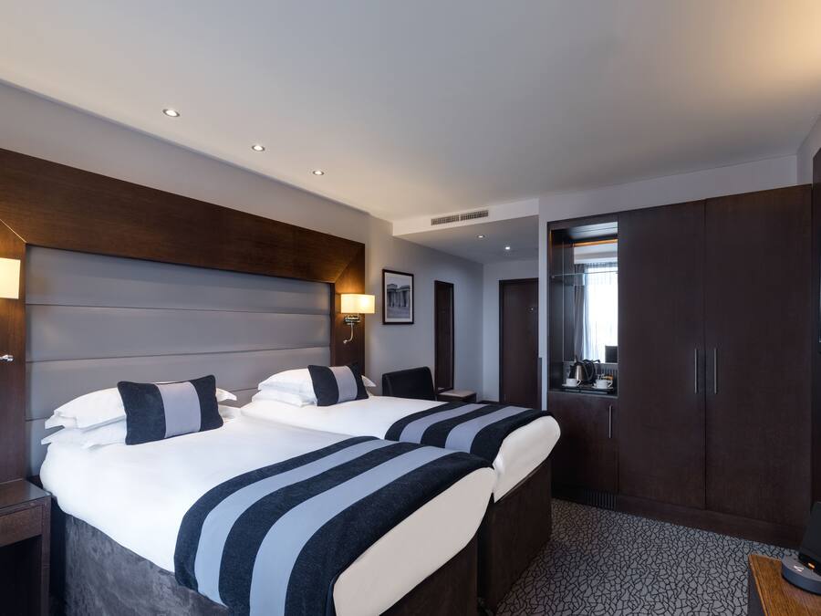 A hotel room with two beds, a desk, a TV, and a bathroom visible through an open door.