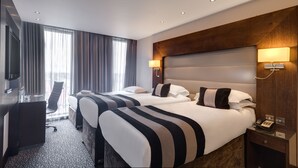 A hotel room with two beds, a desk, a chair, and a TV.