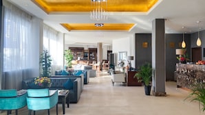 A spacious lobby with a modern design, featuring a seating area with sofas and chairs, a reception desk, and a bar area.