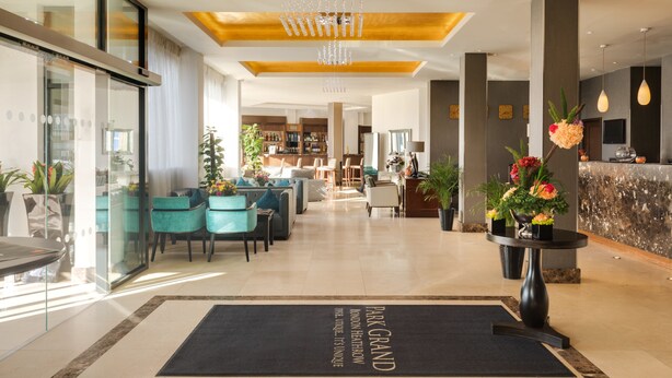 A modern hotel lobby with a reception desk, seating area, and a chandelier.