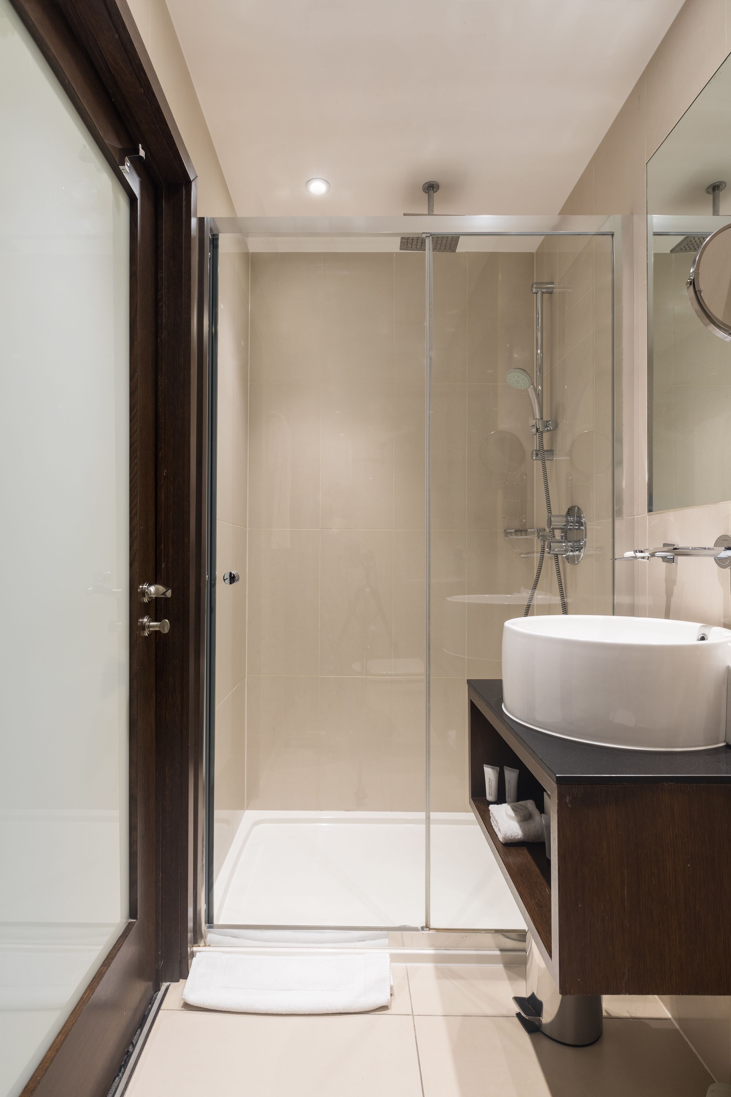 Une salle de bain moderne avec une douche à parois de verre, un lavabo blanc et un meuble-lavabo en bois foncé.