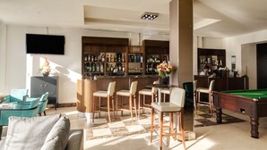 A modern bar area with a pool table, bar stools, and a television mounted on the wall.